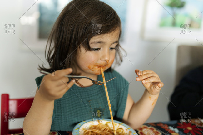 Portrait of little girl with smeared face eating pasta