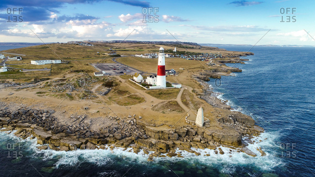 Aerial view of Portland Bill lighthouse with waves crashing on rocks, UK.