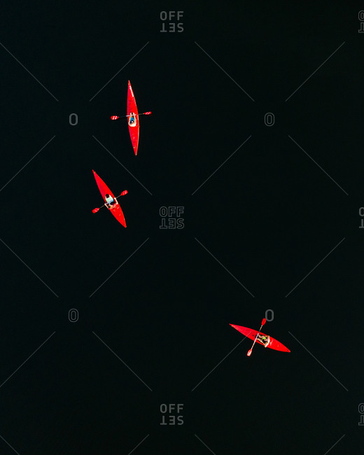 Aerial view of three friends with red kayaks on dark lake water surface in Lithuania.