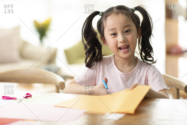 Little Chinese girl cutting paper at home