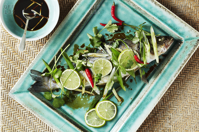Still life with whole roasted bass on serving dish, overhead view