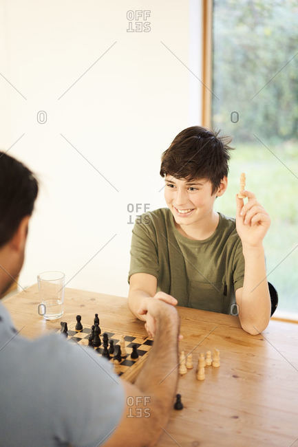 Boy and father shaking hands over game of chess at living room table, over shoulder view