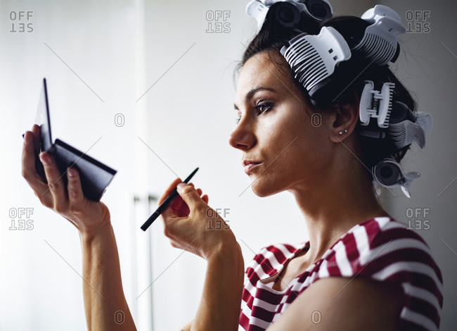 Woman with hair-rollers putting on make up
