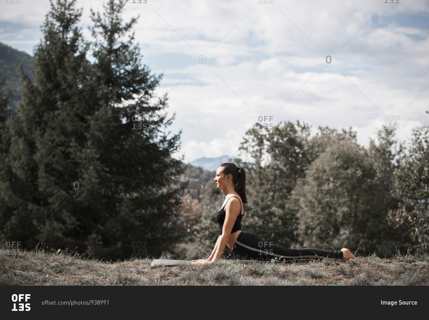 Woman practicing yoga, on yoga mat in rural landscape