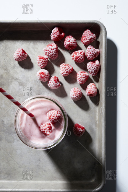 Raspberry yogurt smoothie with frozen raspberries on baking tray, overhead view