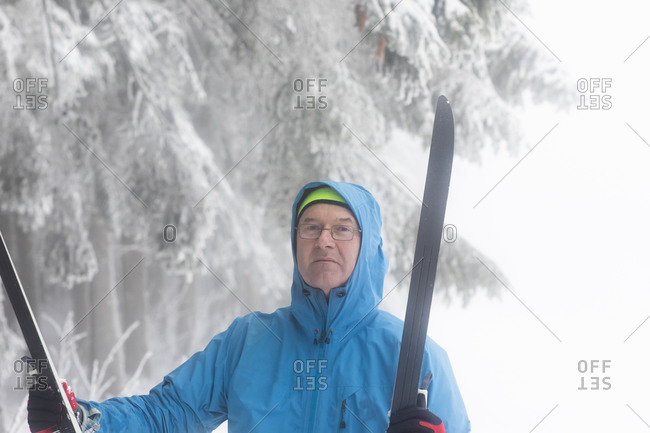 Mature man holding cross country skis by misty forest, portrait