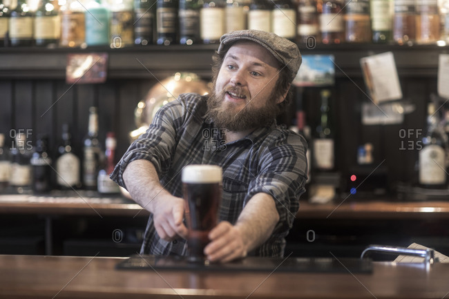 Barman serving beer from bar in traditional Irish public house