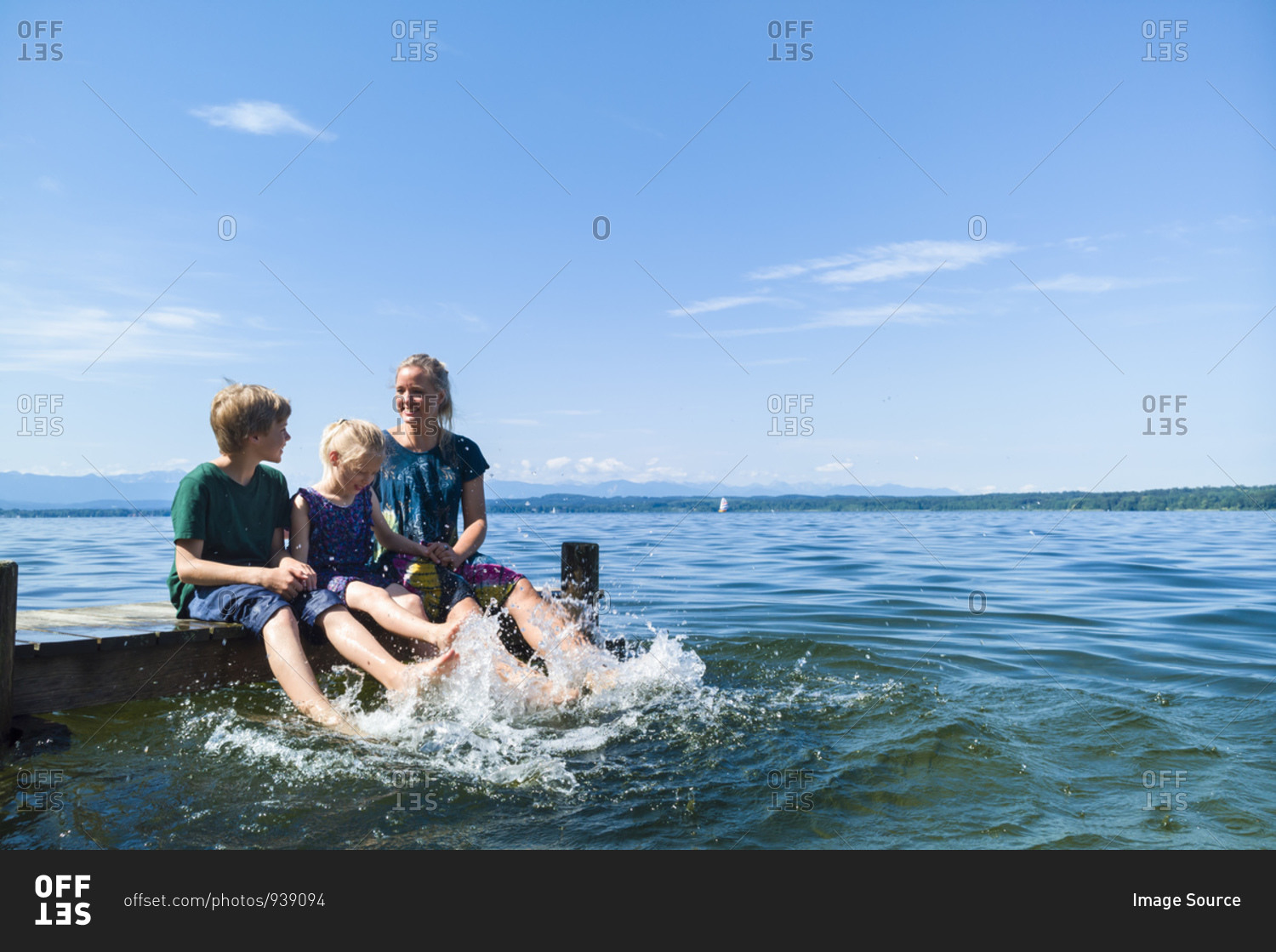 Mother and children cooling feet in water, Lake Starnberg, Bavaria, Germany
