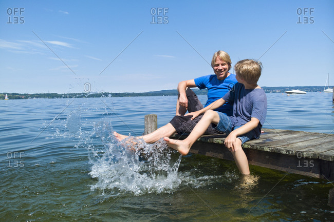Father and son cooling feet in water, Lake Starnberg, Bavaria, Germany