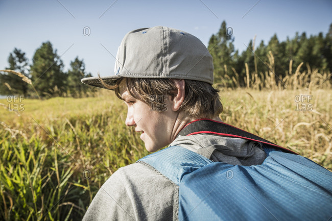 Teenage boy with backpack in field of long grass, Sandpoint, Idaho, USA