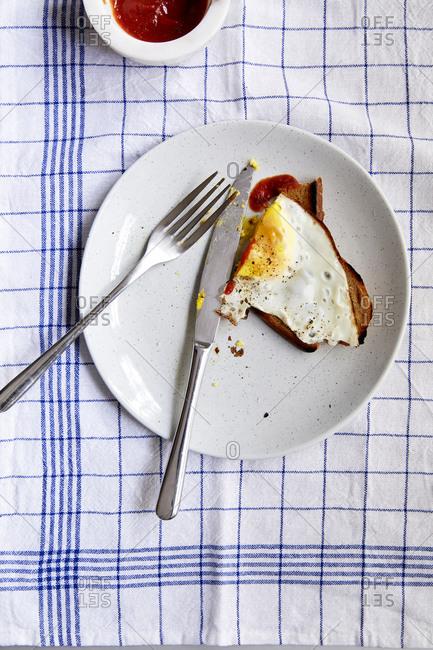 A fried egg on toast on a plate with utensils and tomato sauce,