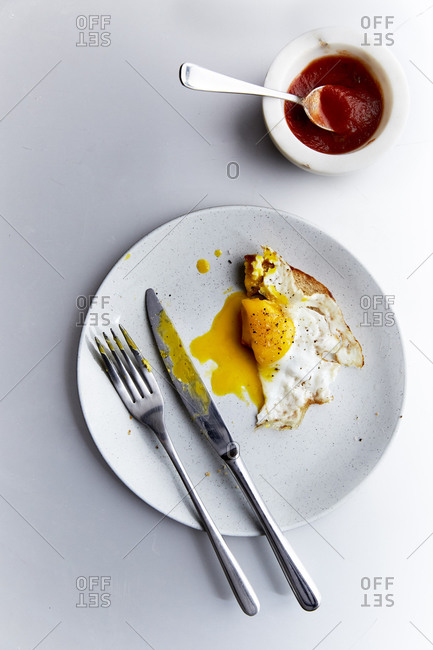 A fried egg on toast on a plate with utensils and tomato sauce,