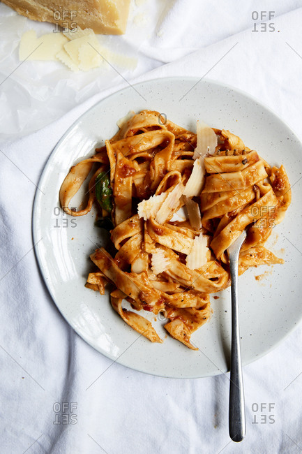 Pasta in a creamy tomato sauce and freshly shaved parmesan on a plate and a white background,