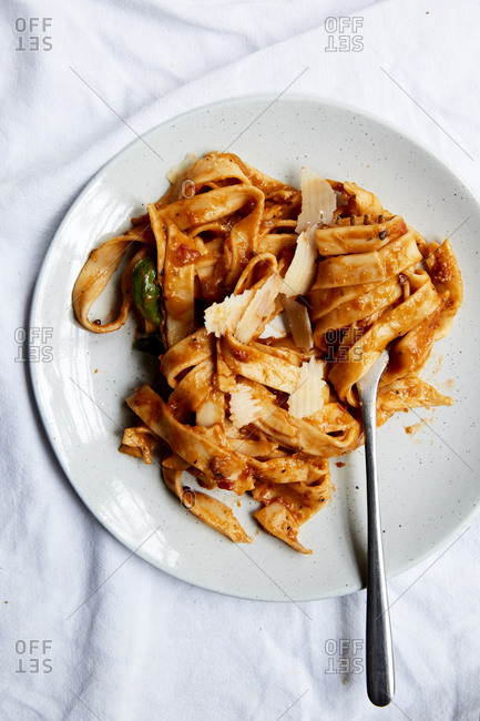 Pasta in a creamy tomato sauce and freshly shaved parmesan on a plate and a white background,