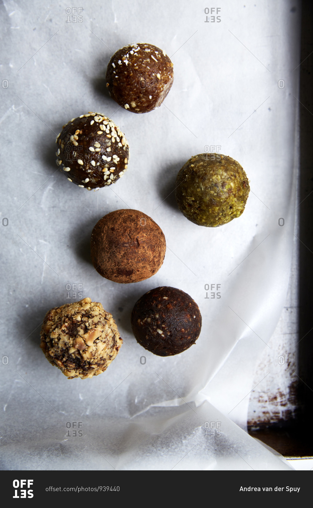 Different types of date balls laid out on wax paper in a baking tin,