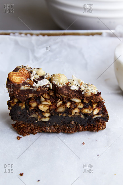 A slice of brownie cake filled with nuts, dates and chocolate on wax paper in a baking tray,