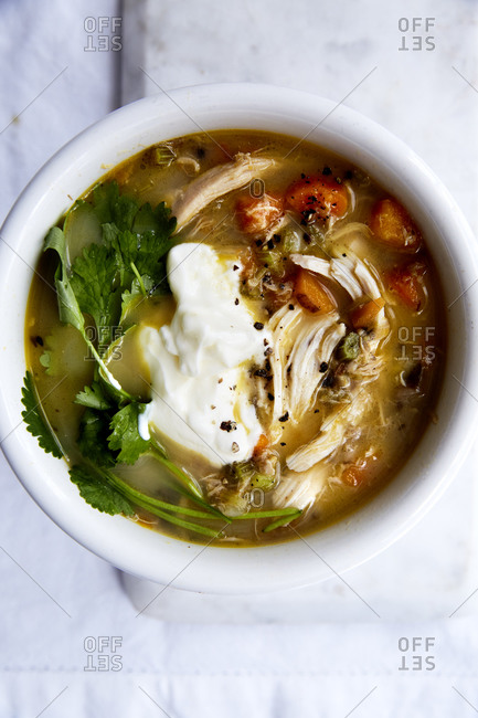 Close up of immune boosting chicken soup with a spoonful of yoghurt and fresh herbs on a light background,