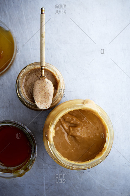 A variety of nut butters and honey in jars with a spoon shot from above,
