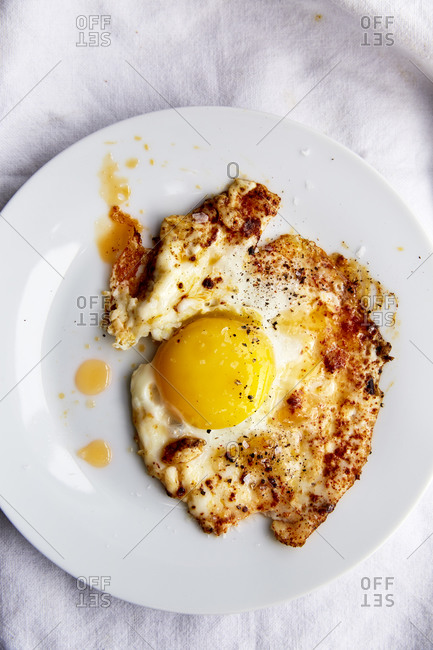 Fried egg in paprika chilli oil in a white plate on a white linen cloth,