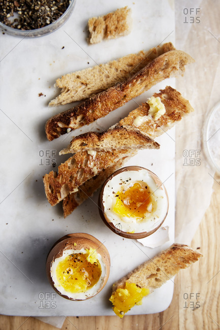 Two soft boiled eggs and toast on the side on a marble serving board,