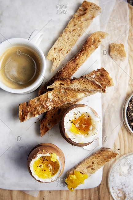 Two soft boiled eggs and toast on the side with an espresso on a marble serving board,
