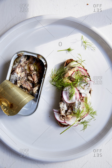 Open tin of sardines with a slice of sardine toast on a white plate,