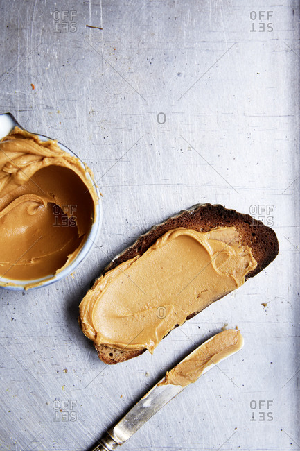 Slice of toast with peanut butter and a spreading knife on a kitchen counter,