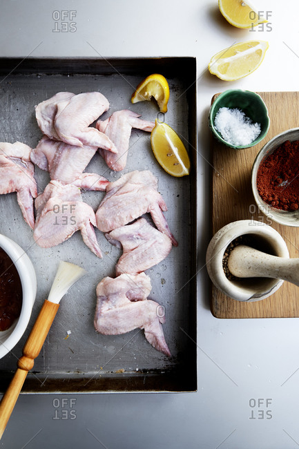 Raw chicken wings on a baking tray with a marinade and a brush with spices on the side,