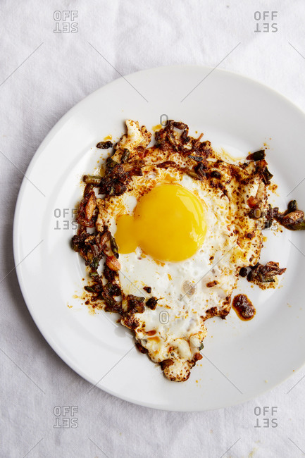 Fried egg in paprika chilli oil in a white plate on a white linen cloth,