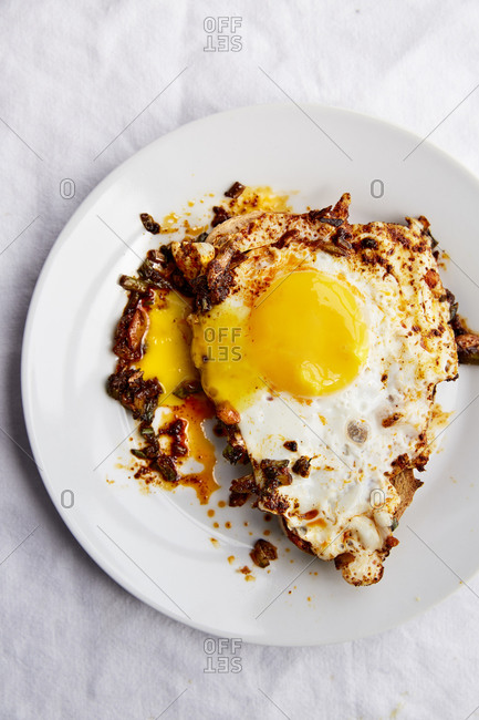 Fried egg on toast with paprika chilli oil in a white plate on a white linen cloth,