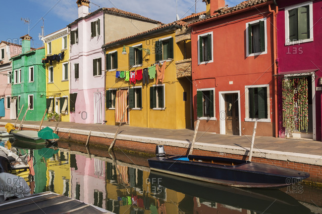 Moored boats on canal lined with pink, red, orange, yellow and green stucco houses decorated with curtains, washed clothes on clothesline, Burano Island, Venetian Lagoon, Veneto, Italy