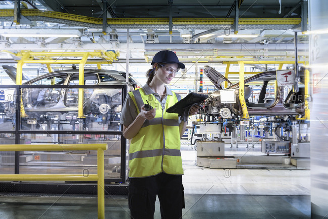 Composite image of female worker with digital tablet in car factory