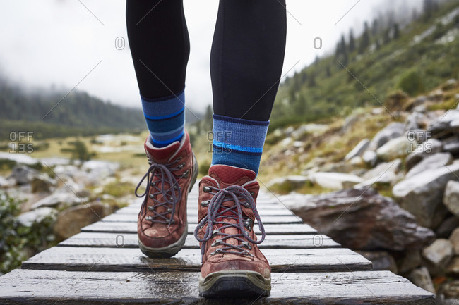 Female hiker hiking across wooden footbridge, cropped view of legs and hiking boots
