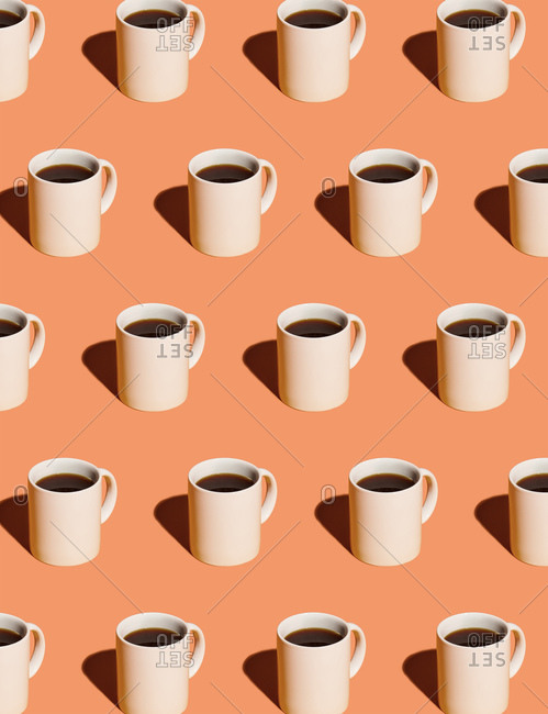 Mugs of black coffee in rows against peach background