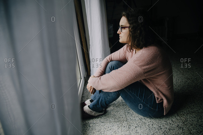 Woman with glasses sitting on the floor looking out the window