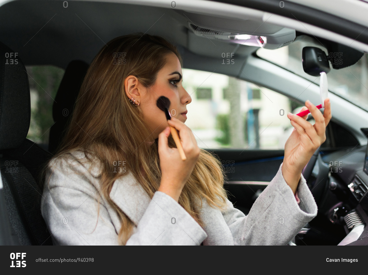 Young woman puts on makeup inside a car