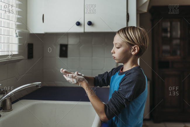 Side view of school aged boy washing hands at home sink