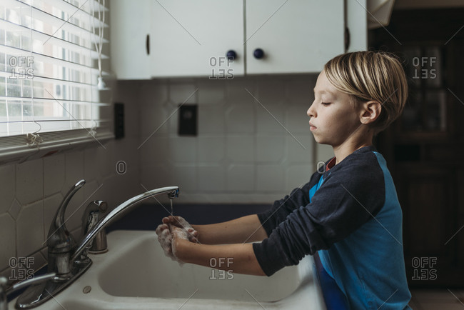 Side view of school aged boy washing hands at sink in kitchen