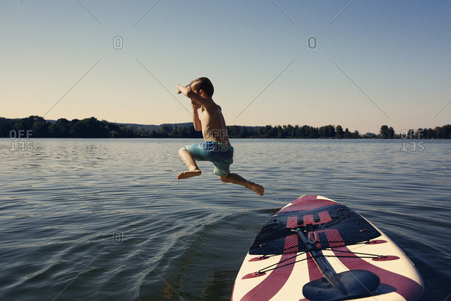 Boy jumping from SUP board into lake at evening twilight