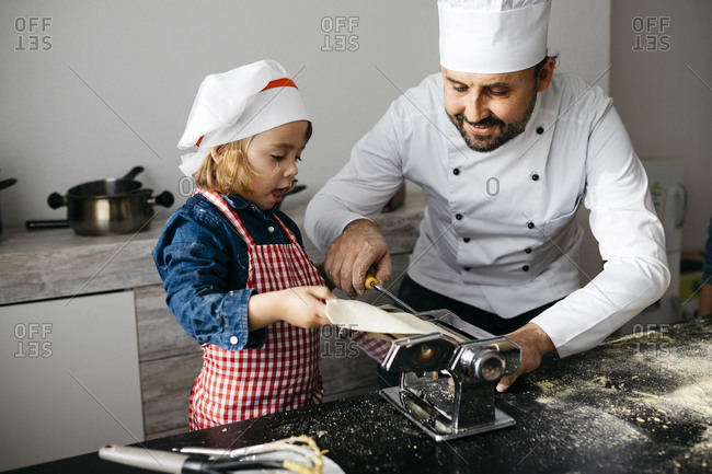 Father and daughter making homemade pasta with pasta machine in kitchen at home