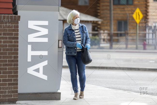 Woman wearing gloves and mask to prevent coronavirus transmission at ATM