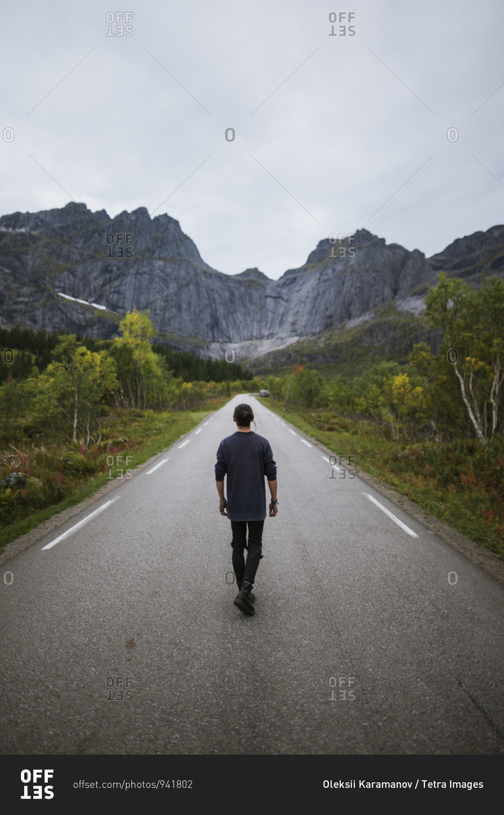Norway, Lofoten Islands, Man walking down road in mountain landscape