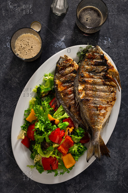 Plate of fried dorado and fresh salad on dark background with glass dark beer top view