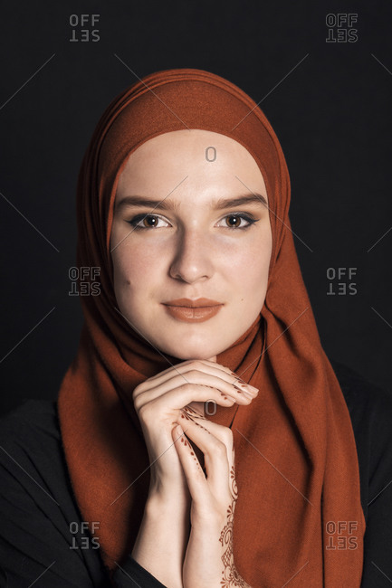 Portrait of a young adult Muslim female wearing brick orange hijab, holding hands under chin