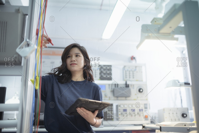 Female electrical engineer standing in front of electrical supply test rig in research facility.