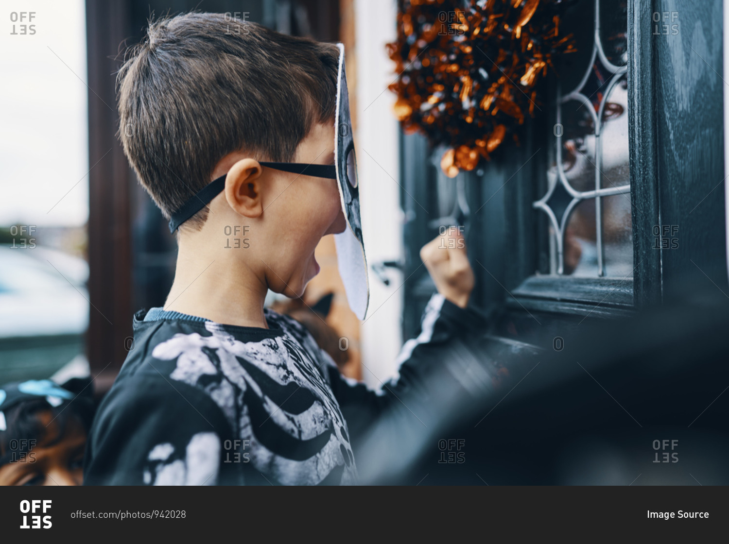 Close up of a boy wearing a mask knocking on a front door at Halloween.