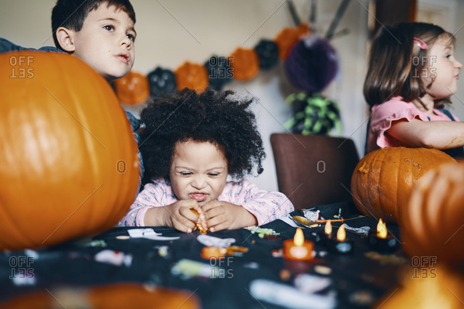 Three children at a table working on making pumpkin heads for Halloween.