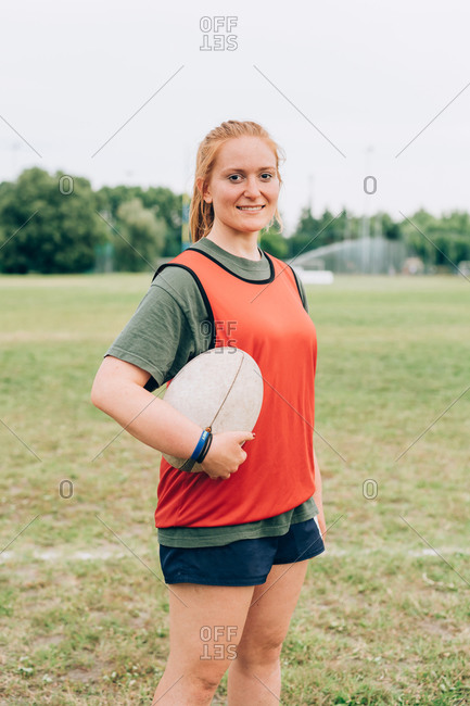 A woman standing on a training pitch in shorts and tee shirt holding a rugby ball.