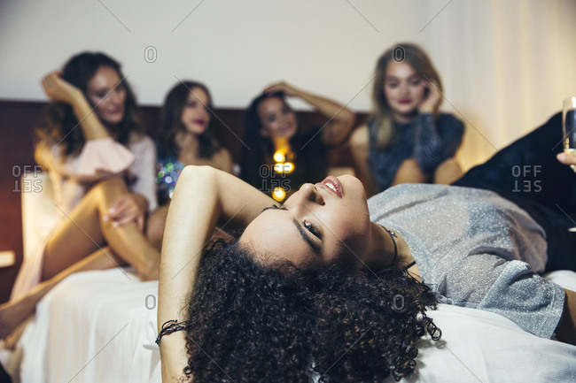 Five women dressed to go out for the evening sitting and lying on a bed.