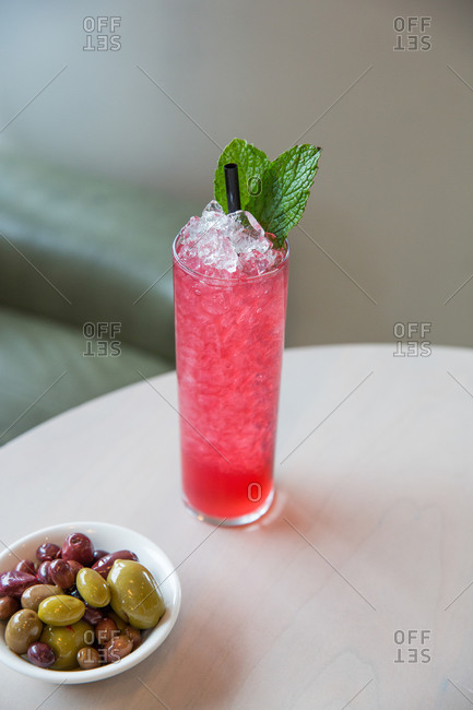 Fancy pink cocktail served by a bowl of olives